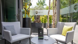 Un espace extérieur moderne, aménagé avec deux fauteuils gris à revêtement rembourré et une petite table ronde, et doté d’un code QR pour accéder à une application mobile.