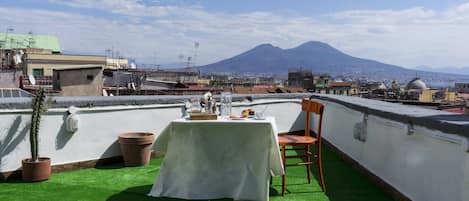 A rooftop terrace with a table set for two, overlooking a cityscape and a mountain.