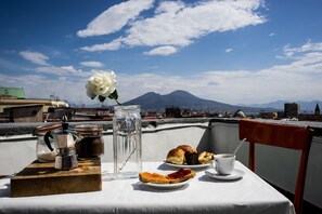 Mesa com comida e bebida num varanda com vista para uma paisagem urbana e uma montanha ao fundo.