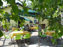 Un área de café al aire libre con mesas y sillas, un edificio con un letrero y follaje en primer plano.