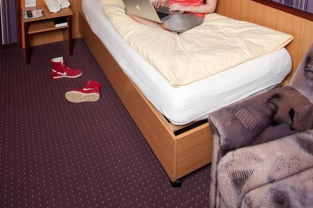 A hotel room with a bed, a desk with a lamp, a chair, and a painting on the wall.