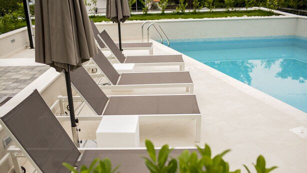 A poolside area with sun loungers and umbrellas, a clear blue pool, and a tiled deck. - Apartments Bago (Split)