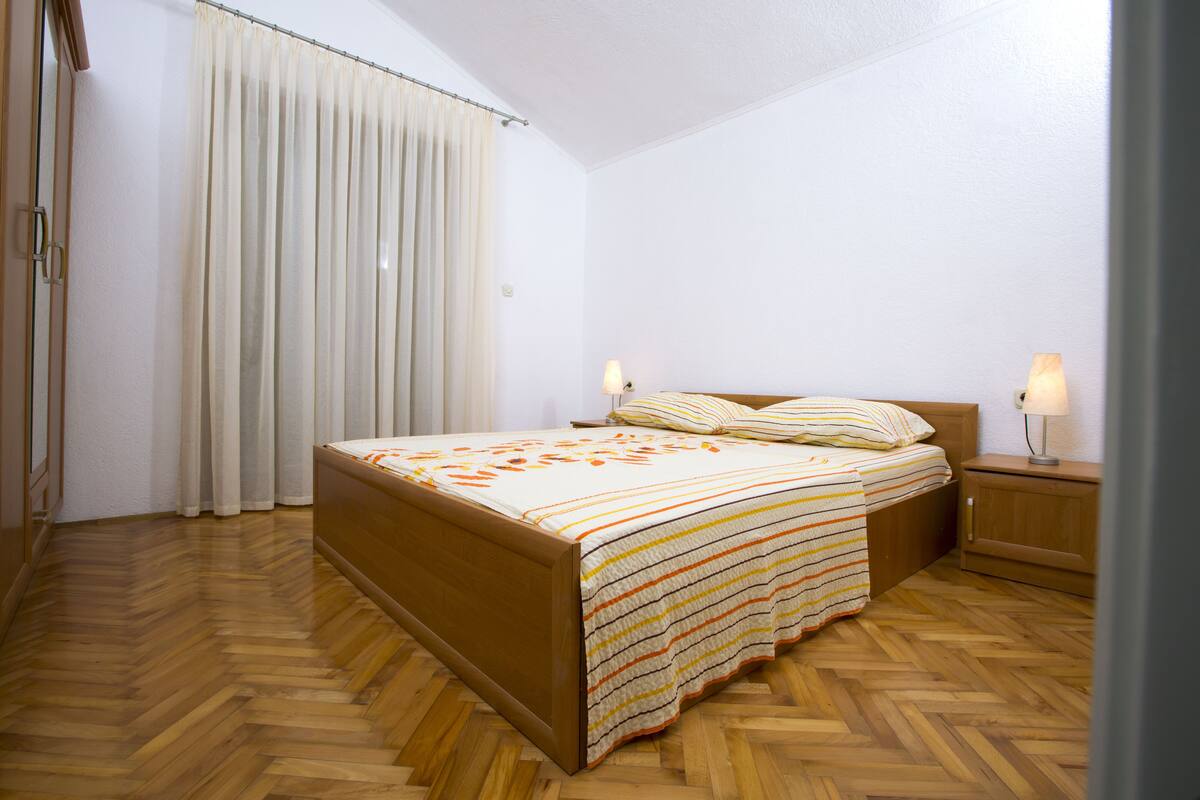A bedroom with a wooden bed, white curtains, and two bedside lamps.