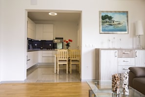 Une cuisine moderne avec des meubles blancs, un coin repas avec une table et des chaises en bois, et un salon avec un canapé et un tableau au mur.