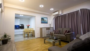 A modern living room with a sofa, a glass coffee table, a dining area with a table and chairs, and a kitchen in the background. - Apartments Bago (Split)
