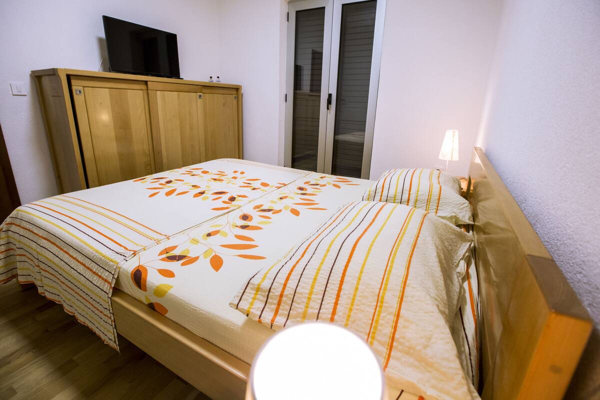 A bedroom with a bed, wooden wardrobe, and a television on the wall.