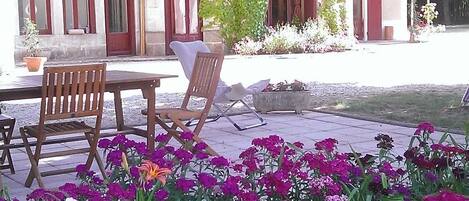A building with a garden area featuring a table and chairs, surrounded by vibrant flowers.