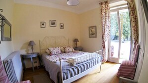 Une chambre à coucher comprenant un lit, deux tables de chevet, un radiateur, une chaise et une fenêtre avec des rideaux.