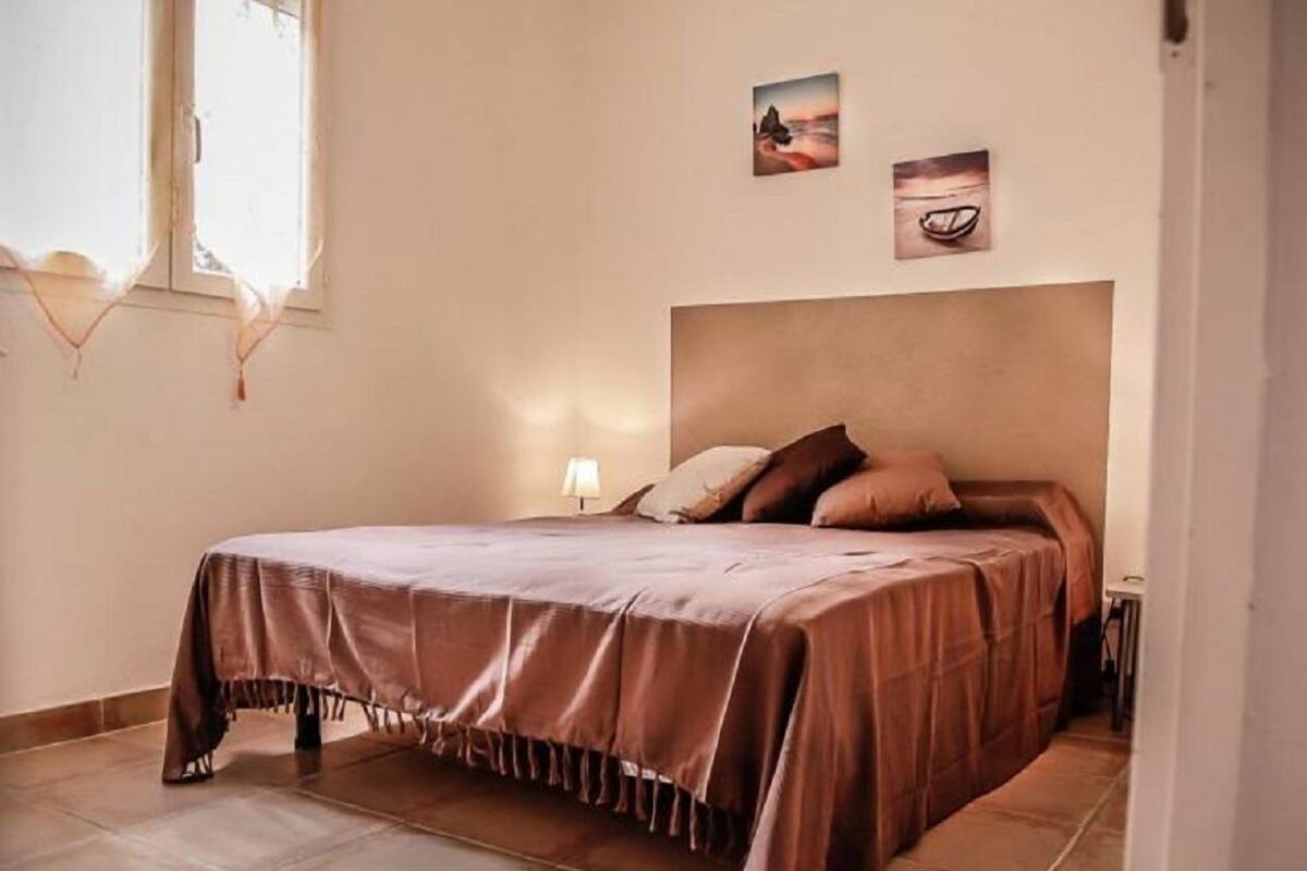 Une chambre à coucher comprenant un lit, une table de chevet, une lampe et deux tableaux accrochés au mur.