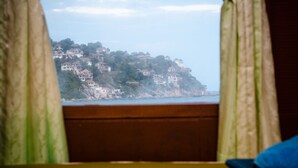 A view from a window with curtains, overlooking a coastal area with houses on a hillside. - OK2 Bungalow (Koh Tao)