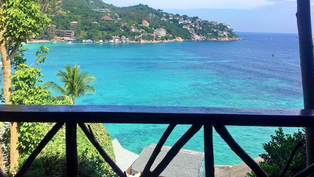 A coastal view with a clear blue sea, a hillside with buildings, and a wooden deck in the foreground. - OK2 Bungalow (Koh Tao)