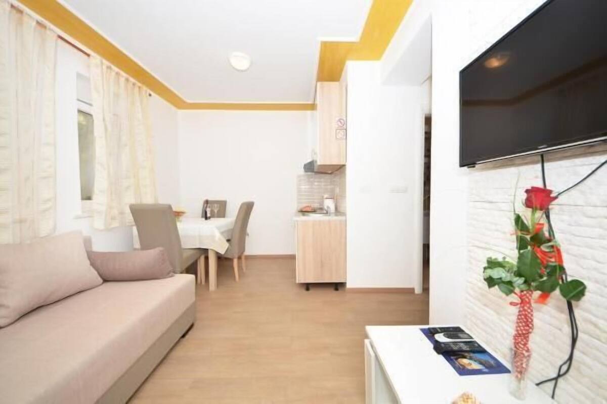 Ein modernes Wohnzimmer mit einer Couch, einem Essbereich mit Tisch und Stühlen, einer Küchenzeile und einem Wand-Fernseher.