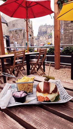 A meal on a wooden table with a newspaper underneath, set outdoors with wooden chairs and red umbrellas. - Kick Ass Greyfriars - Adults Only - Hostel (Edinburgh)