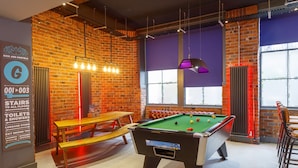 A pool table in a room with brick walls, a wooden bench, and a table lamp.