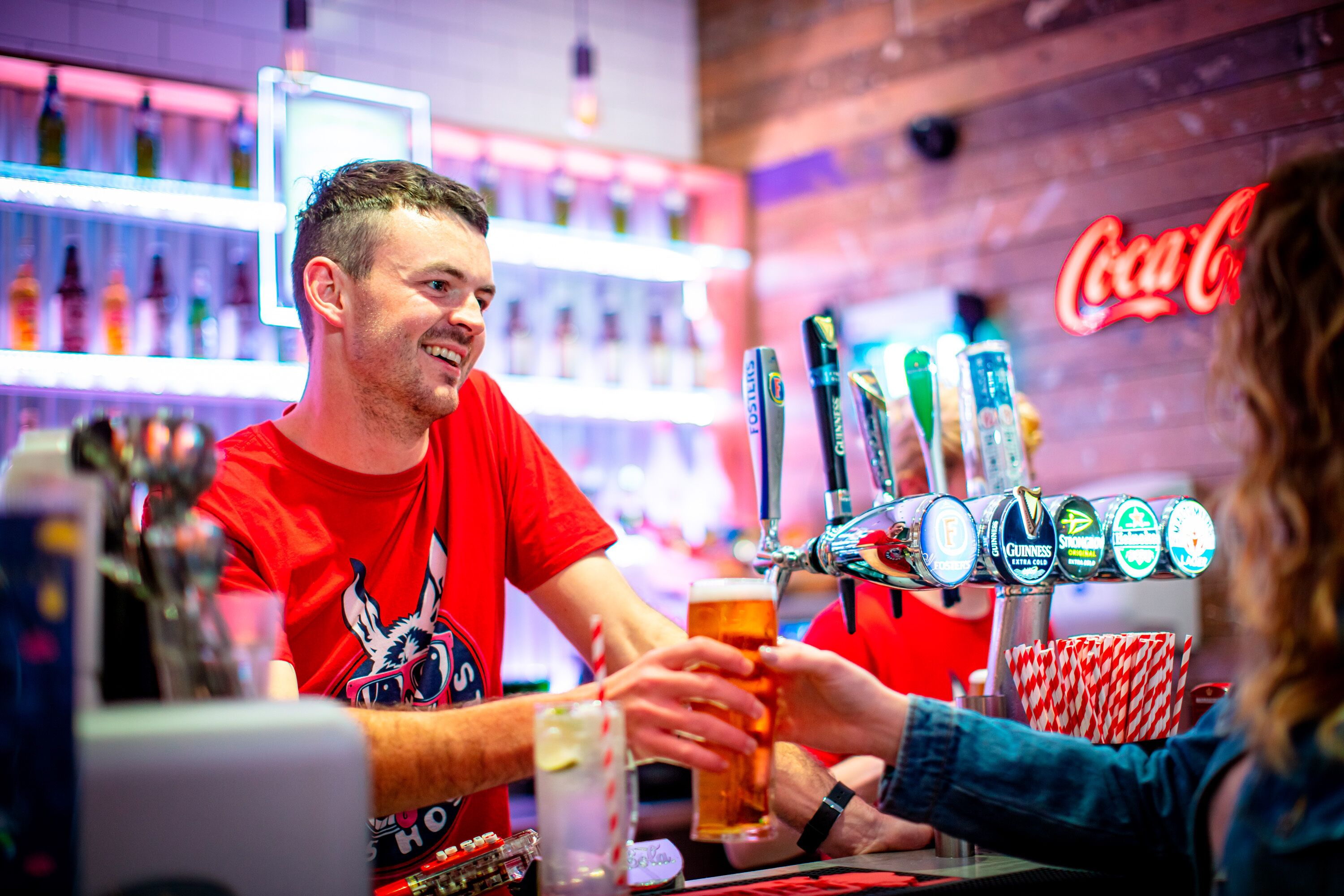 A bar with multiple beer taps and a neon sign in the background.
