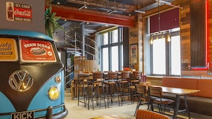 A vintage VW bus interior converted into a restaurant with tables and chairs, a staircase, and a Coca-Cola sign.