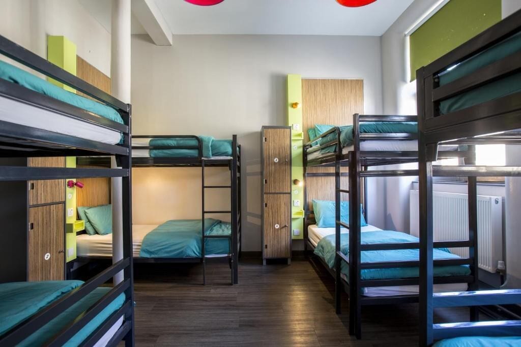 A compact dormitory room with bunk beds, a wardrobe, and a radiator.