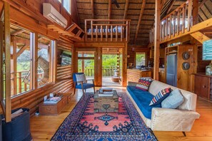 A log cabin with a wooden interior, a sofa, a dining table, and a kitchen area. - Mountain Cabin (Wolseley)