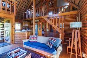 A log cabin interior with a sofa, wooden staircase, and a dining area. - Mountain Cabin (Wolseley)