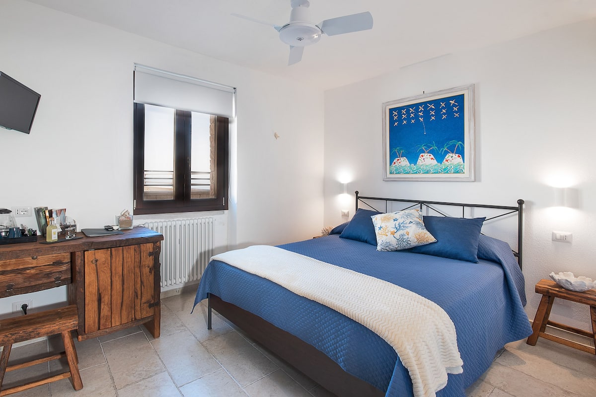 Ein Schlafzimmer mit Bett, Schreibtisch, Stuhl, Fenster und Deckenventilator.