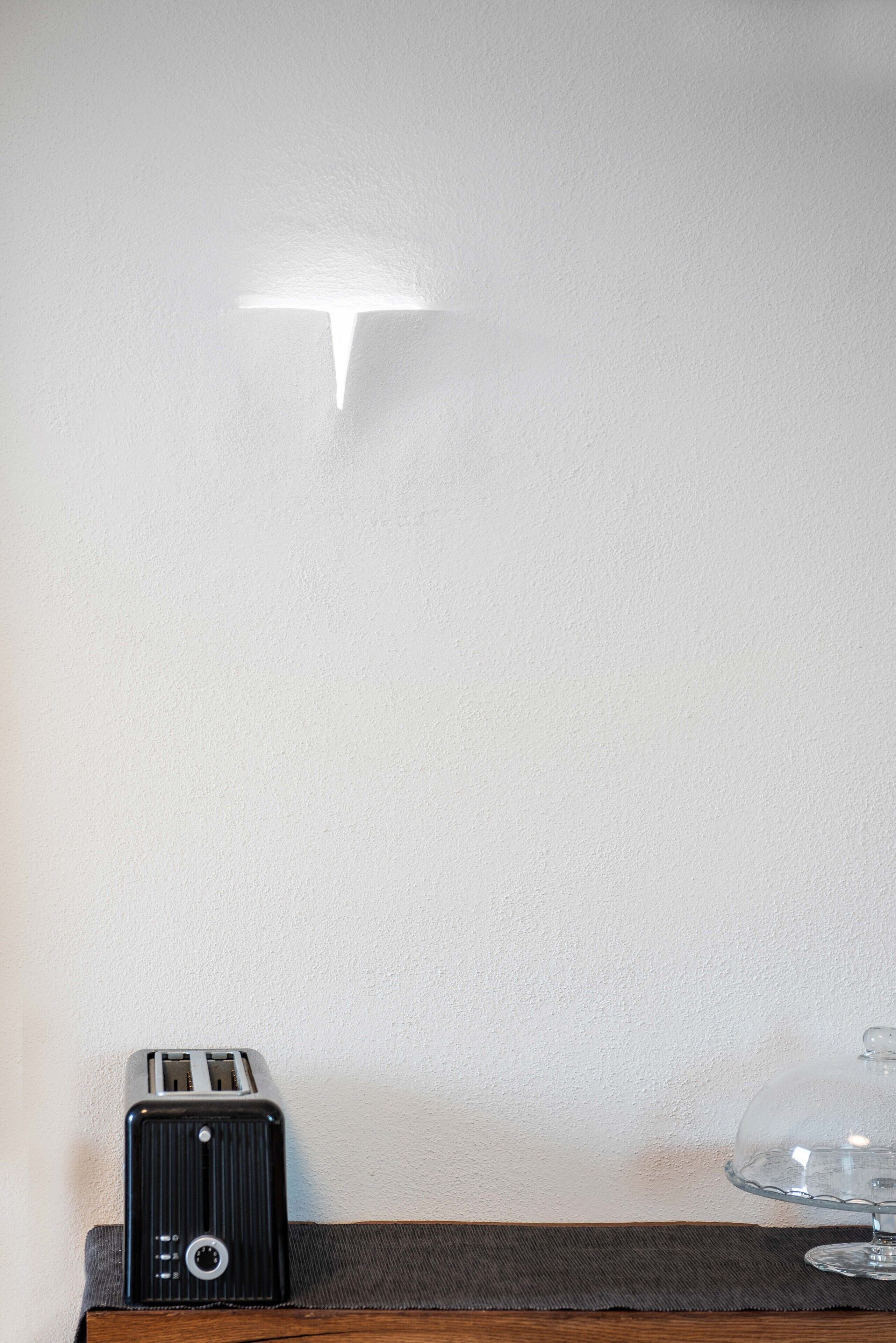 Un grille-pain noir d’époque, posé sur une table en bois devant un mur blanc, avec un luminaire.