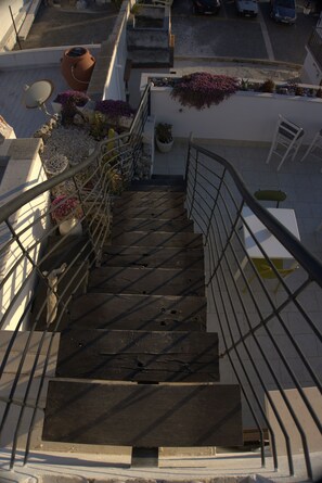 Un escalier avec des rampes en métal, menant à un balcon agrémenté de plantes en pot et offrant une vue sur les voitures garées.