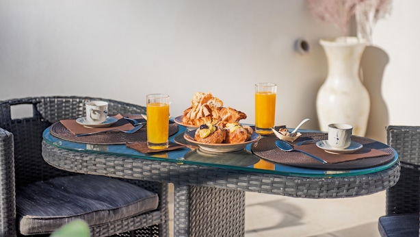 Mesa de vidro redonda com cadeiras de vime, um prato de comida e dois copos de suco de laranja.