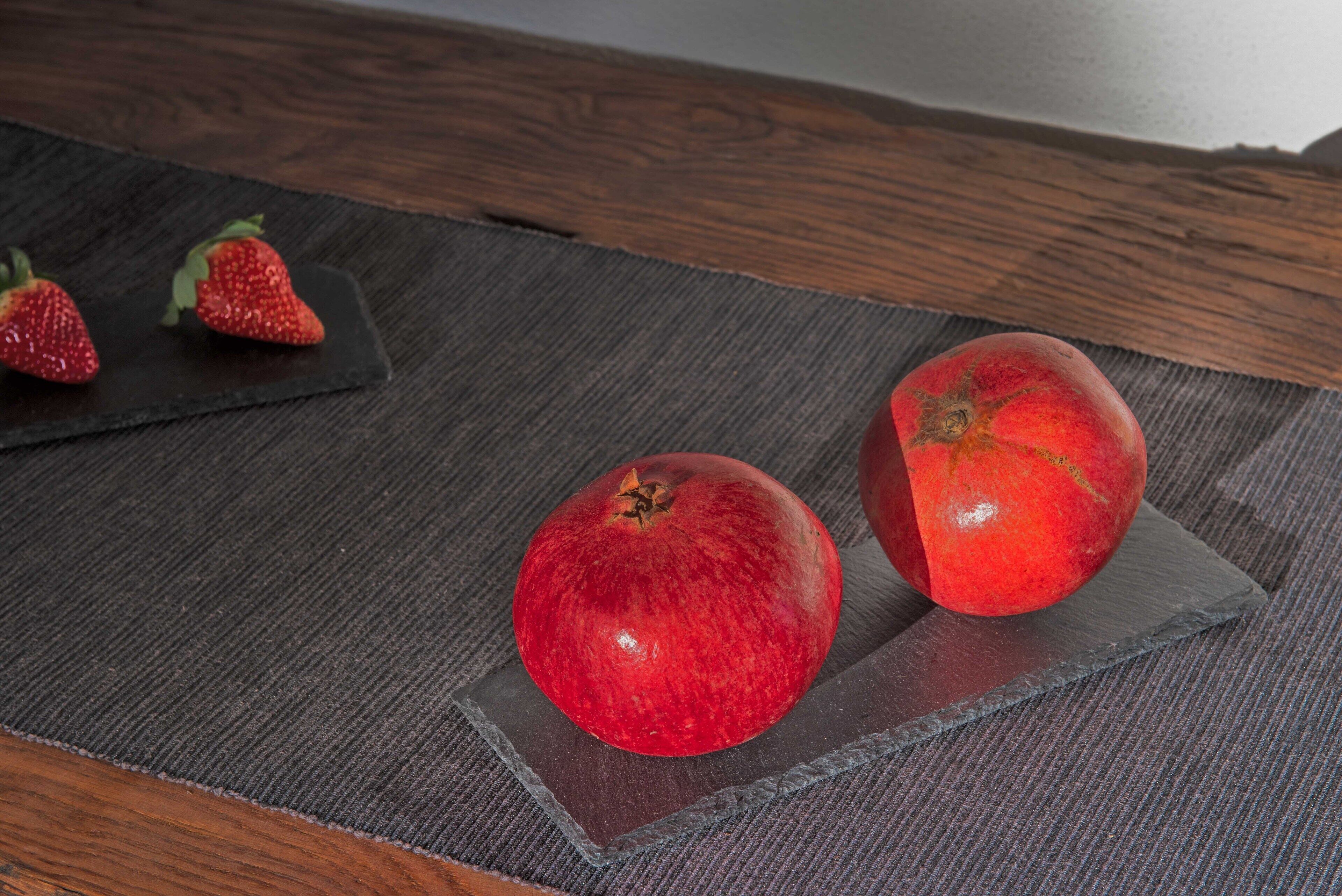 A pomegranate and two strawberries on a dark mat.