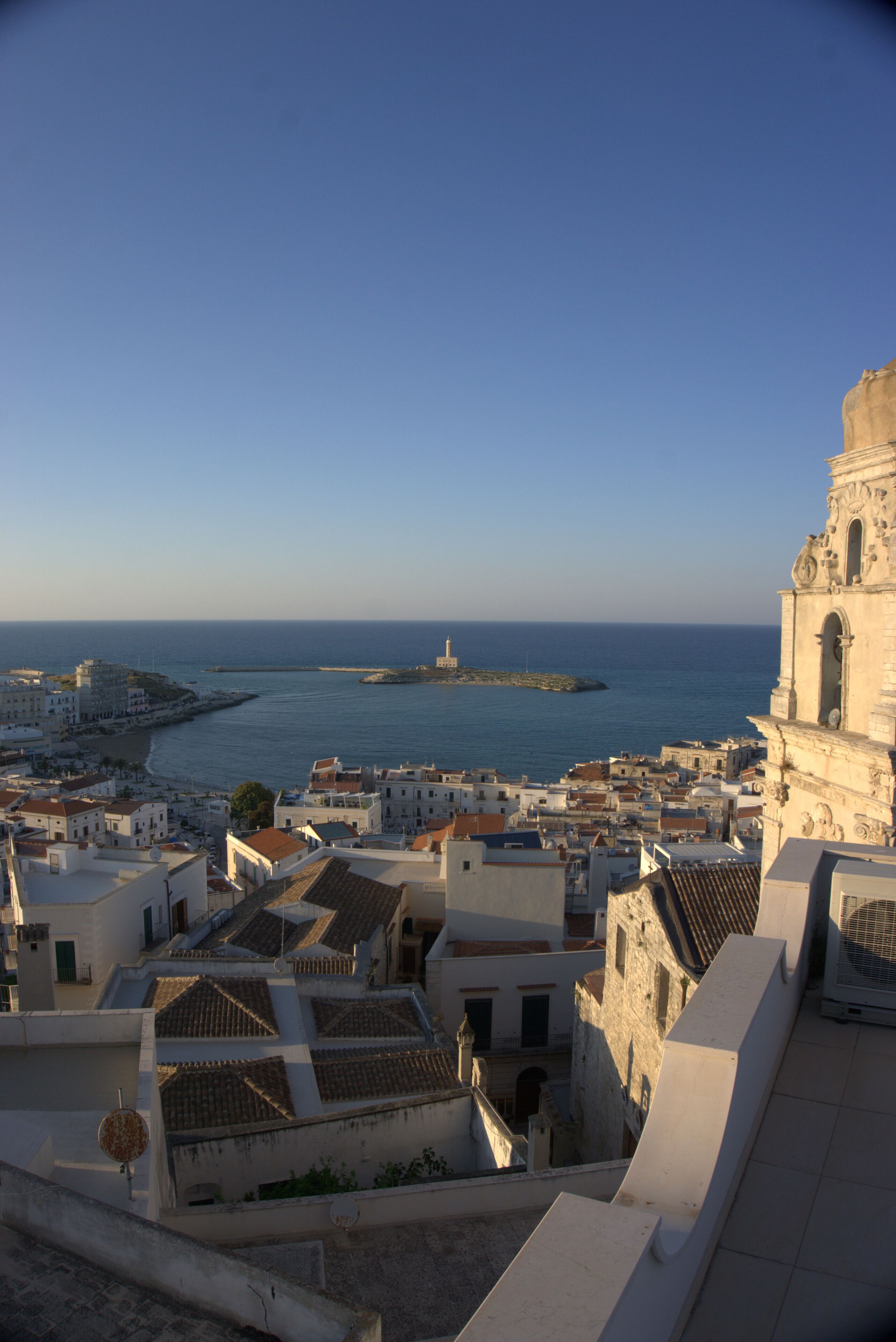Un paysage urbain côtier avec des bâtiments historiques, une église imposante et une vue sur la mer.