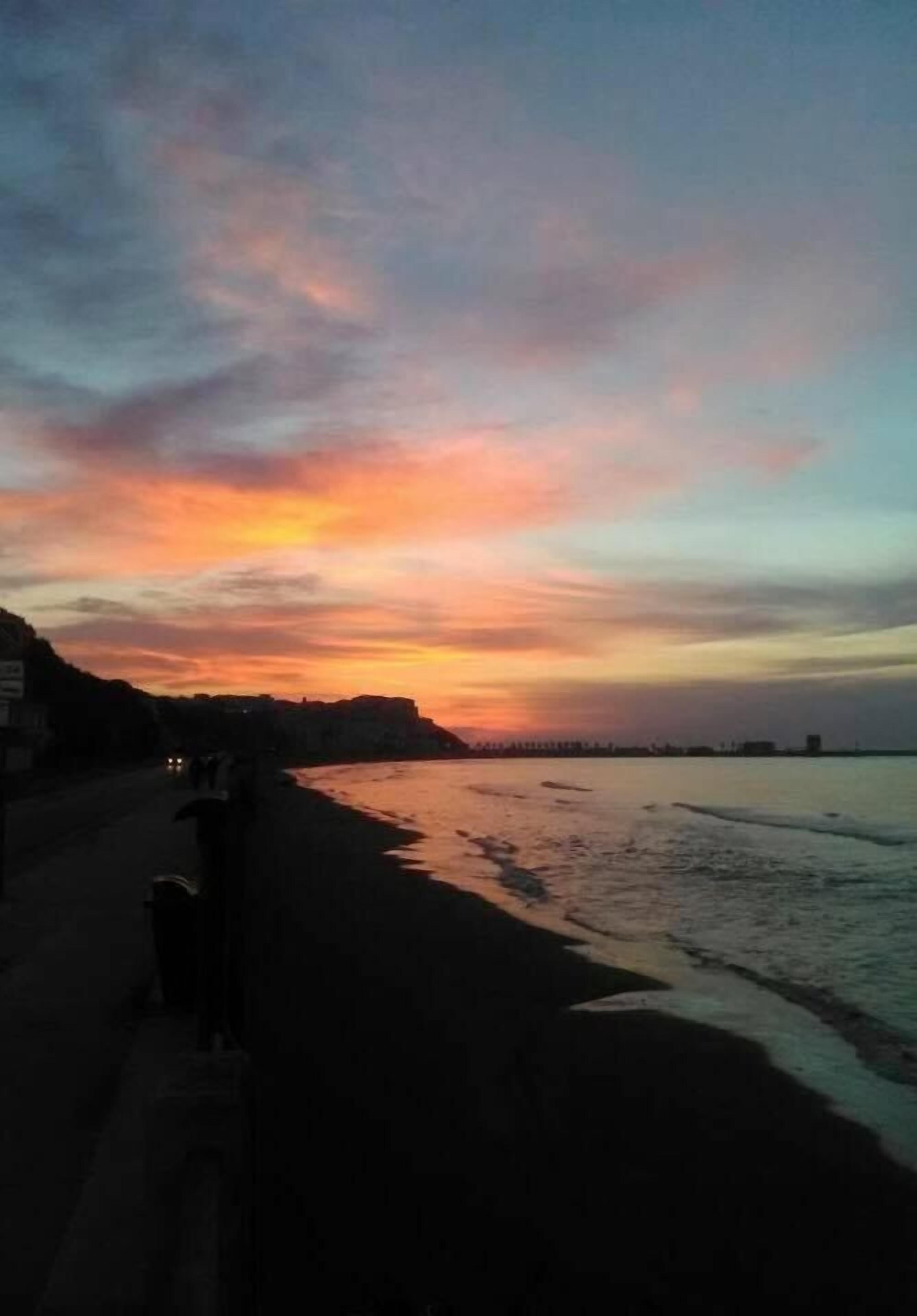 A beach at sunset with a clear sky and calm waters.