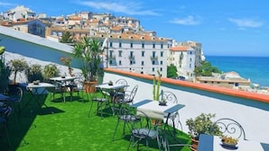 Une terrasse sur le toit avec des sièges extérieurs, une vue sur la mer et des bâtiments en arrière-plan.