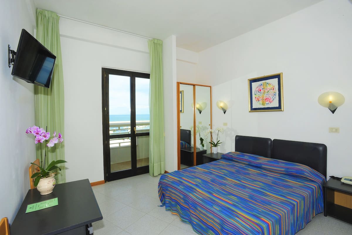 Une chambre d’hôtel avec un lit, un bureau, une télévision, une fenêtre donnant sur un beau paysage et un tableau au mur.