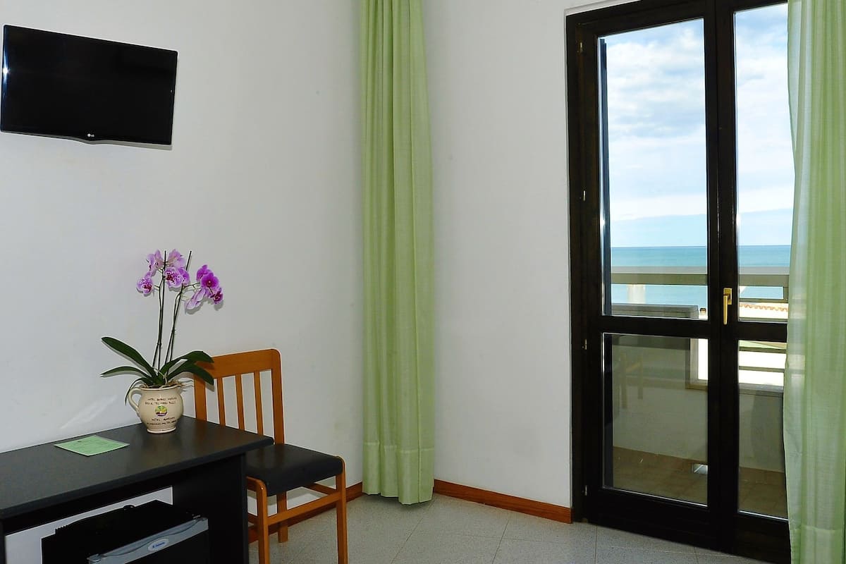 Une chambre dotée d’un bureau, d’une chaise, d’une télévision et offrant une vue sur la mer grâce à une porte coulissante.