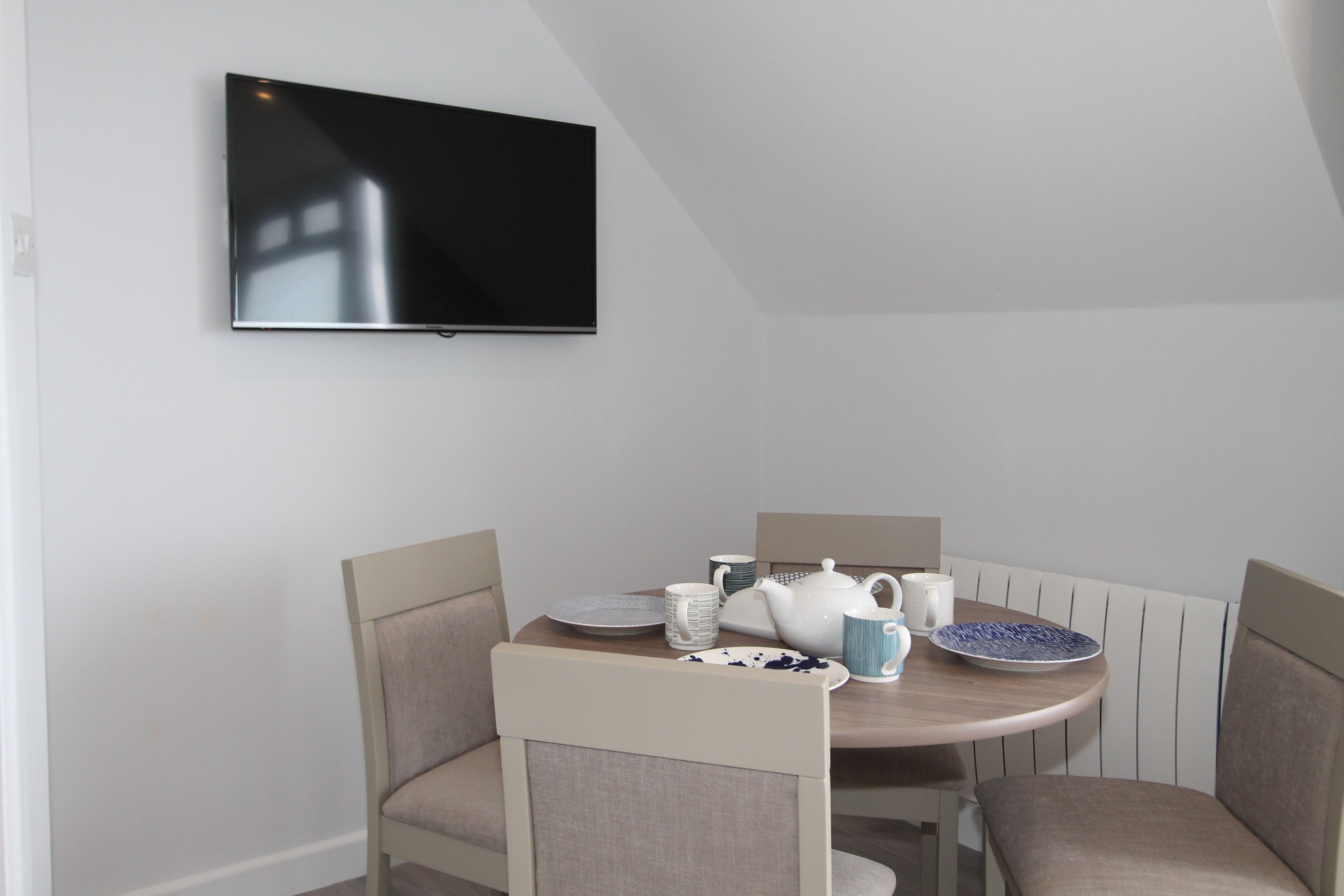 Un coin repas avec une table ronde, des chaises et un téléviseur à écran plat fixé au mur.