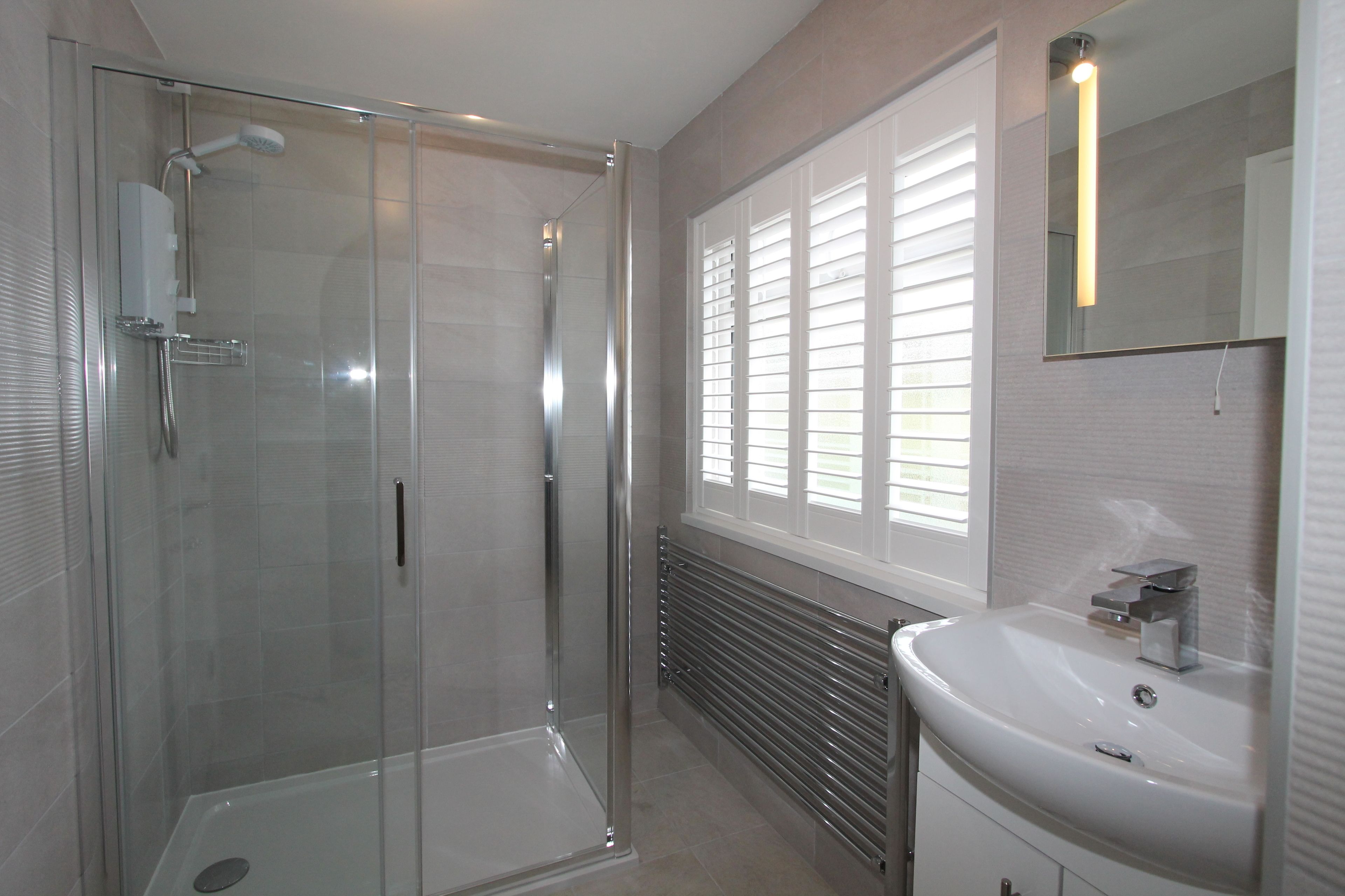 A modern bathroom with a glass-enclosed shower, a white sink, and a large mirror.