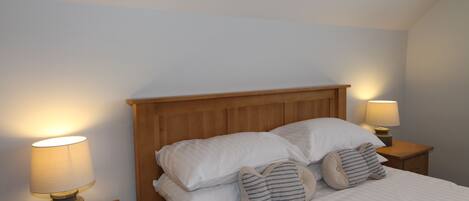 Una cama bien hecha con sábanas blancas y almohadas a rayas, con dos lámparas de noche de madera a cada lado.