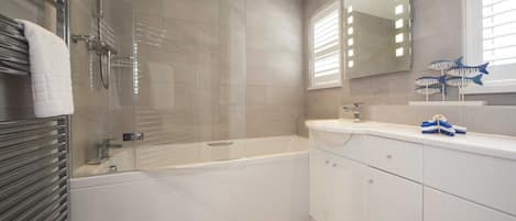 A modern bathroom with a glass-enclosed shower, a freestanding bathtub, and a vanity with a mirror and fish-shaped soap holders.