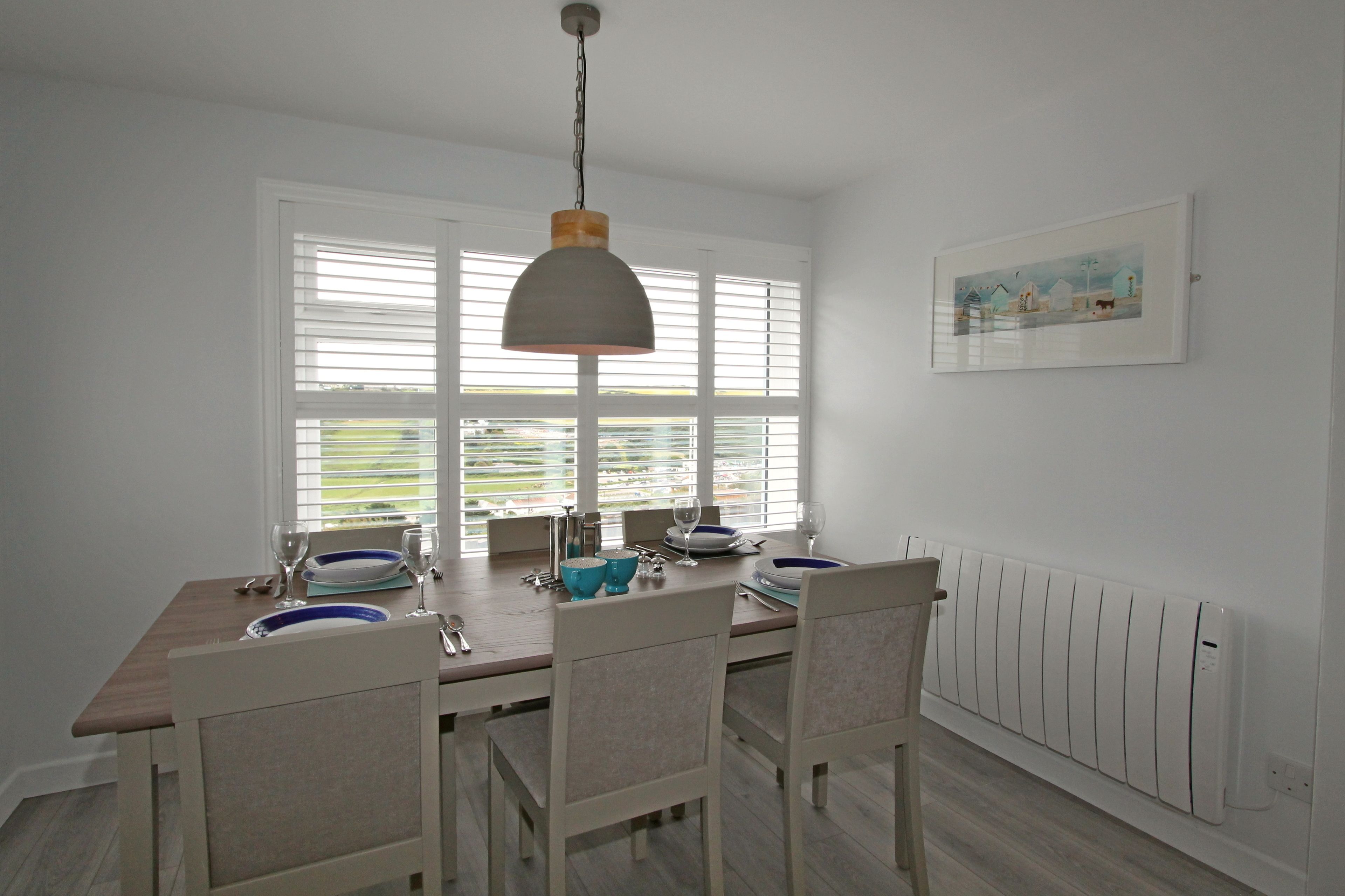 A dining area with a table set for four, white chairs, a pendant light, and a radiator on the wall.