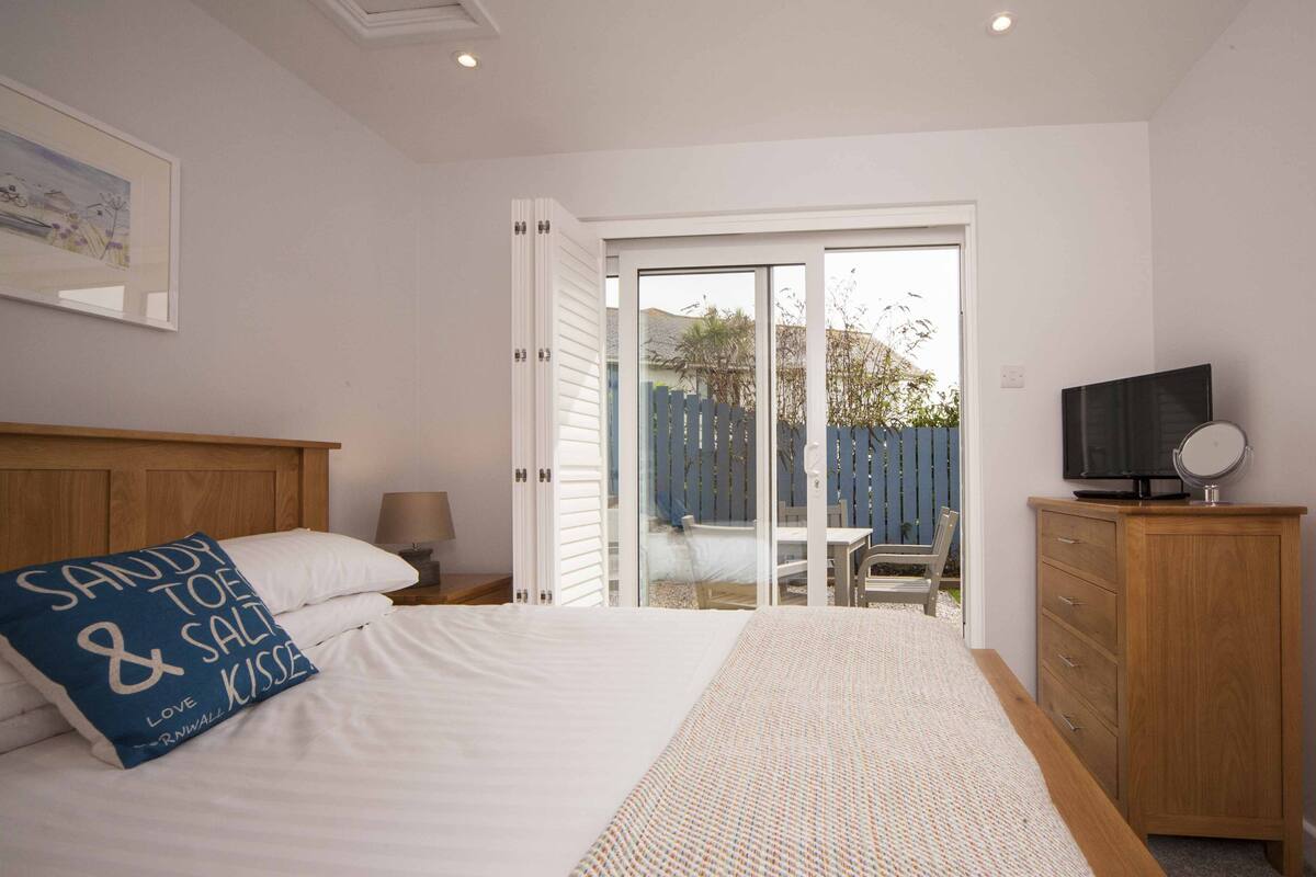 Een slaapkamer met een bed, een televisie, een houten kast en een schuifdeur naar een buitenruimte.