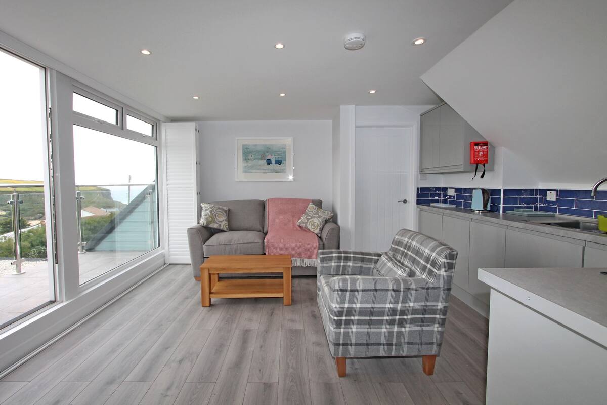Een moderne keuken met een inbouwfornuis, een eethoek met een houten tafel en een grote schuifpui die leidt naar een balkon met uitzicht op het landschap.