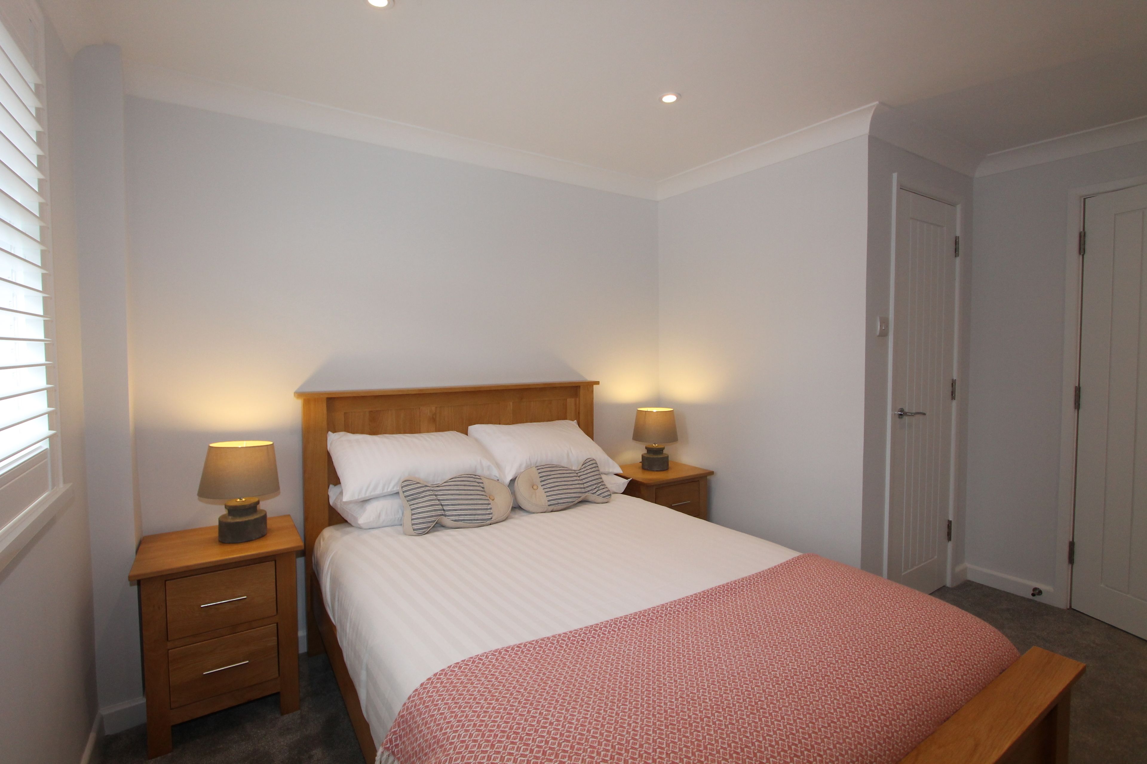 Une chambre à coucher avec un lit, deux tables de chevet avec des lampes, une tête de lit en bois et une porte.