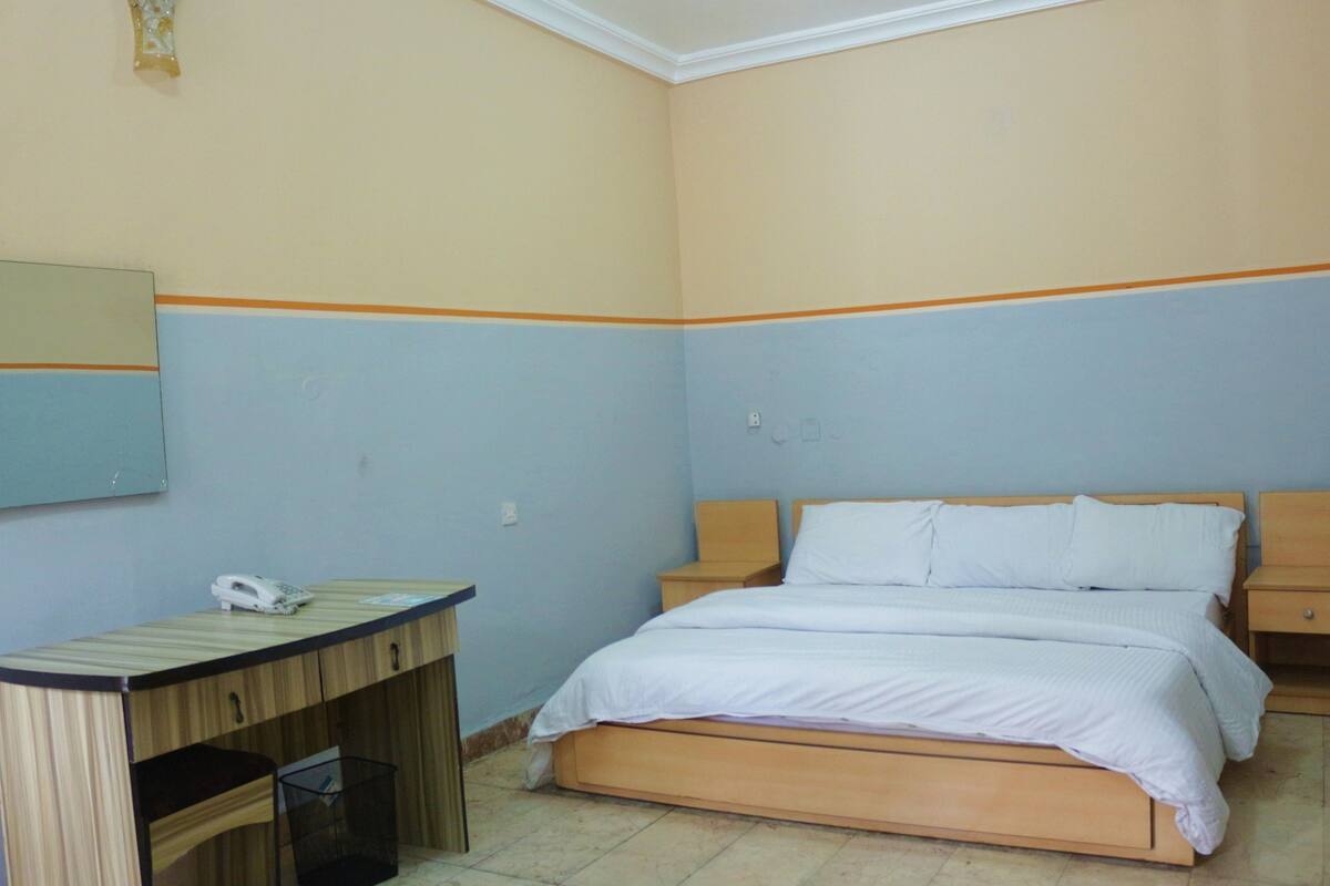 A bedroom with a bed, bedside tables, a desk, and a mirror.