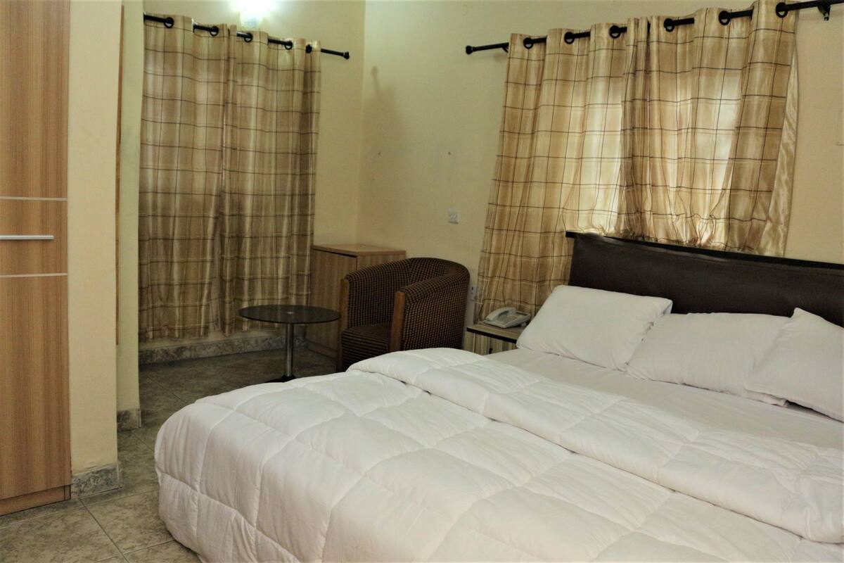 A bedroom with a bed, a chair, a small table, and curtains.