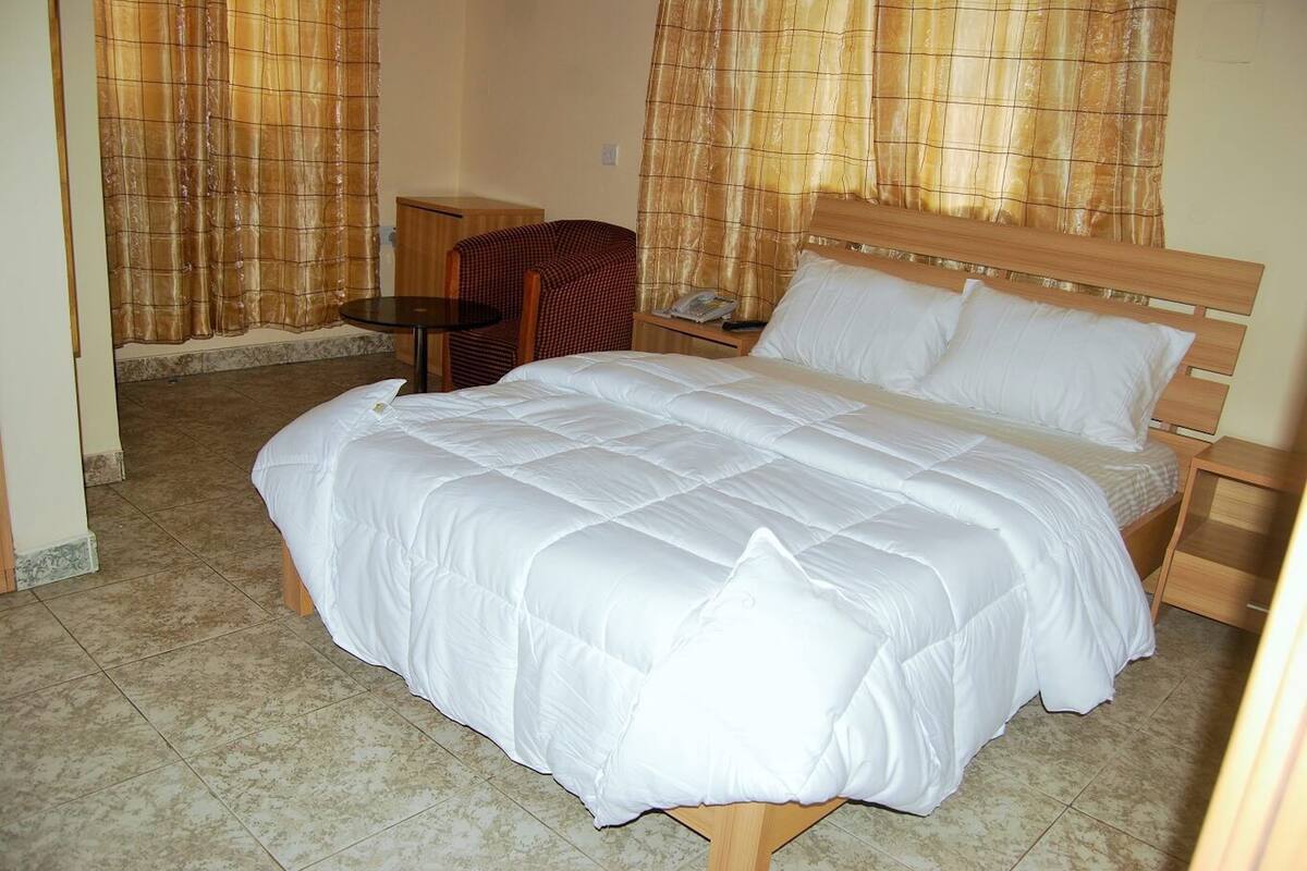 A hotel room with a large bed, a wooden headboard, a small table, and a chair.