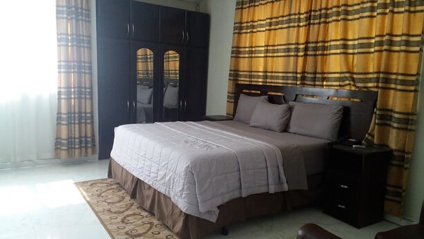 A bedroom with a bed, a wardrobe, a nightstand, and a patterned rug. - White Stone Lodge (Accra)