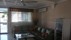 A living room with a sectional sofa, a glass coffee table, and a built-in refrigerator. - White Stone Lodge (Accra)