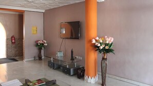 A reception area with a modern reception desk, a large orange pillar, and two vases with flowers. - White Stone Lodge (Accra)