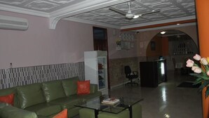 A living room with a green sofa, a glass coffee table, and a ceiling fan. - White Stone Lodge (Accra)