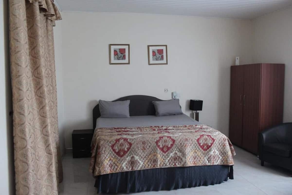A bedroom with a bed, two framed pictures on the wall, a wardrobe, and a nightstand.