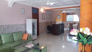 A hotel lobby with a green sofa, a glass coffee table, a reception desk, and a dining area with a table and chairs. - White Stone Lodge (Accra)